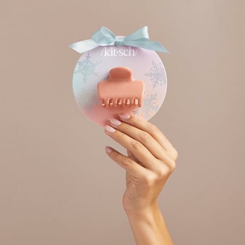 A hand holding a peach-colored hair clip on a circular card with a bow.